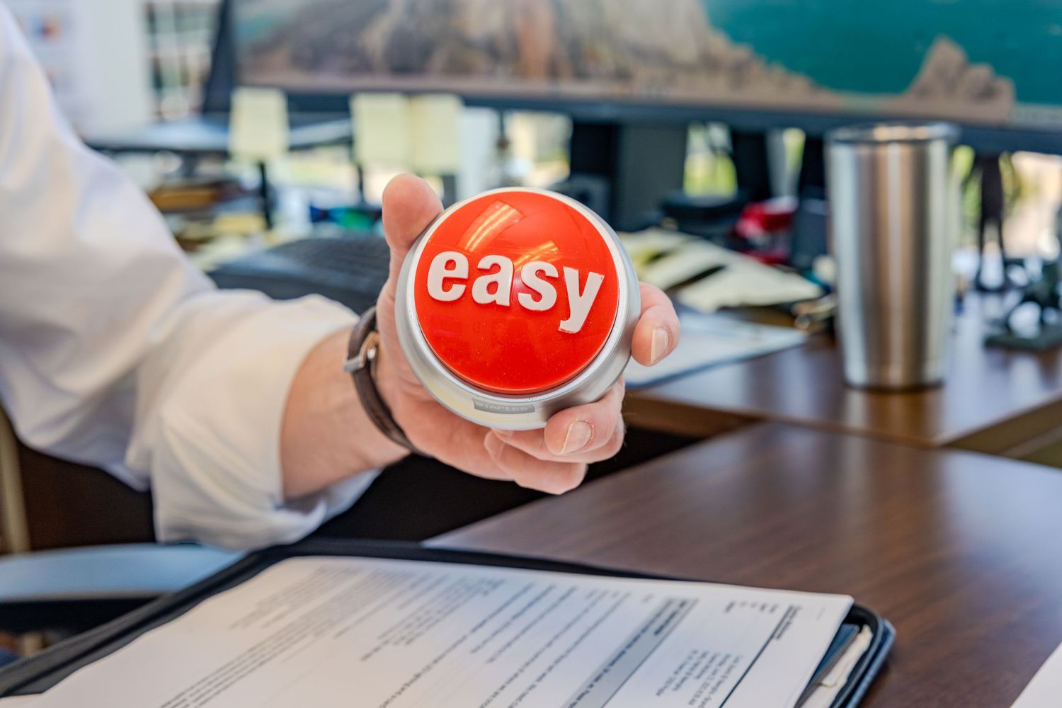 Person holding a red 'easy' button while reviewing paperwork at a desk.