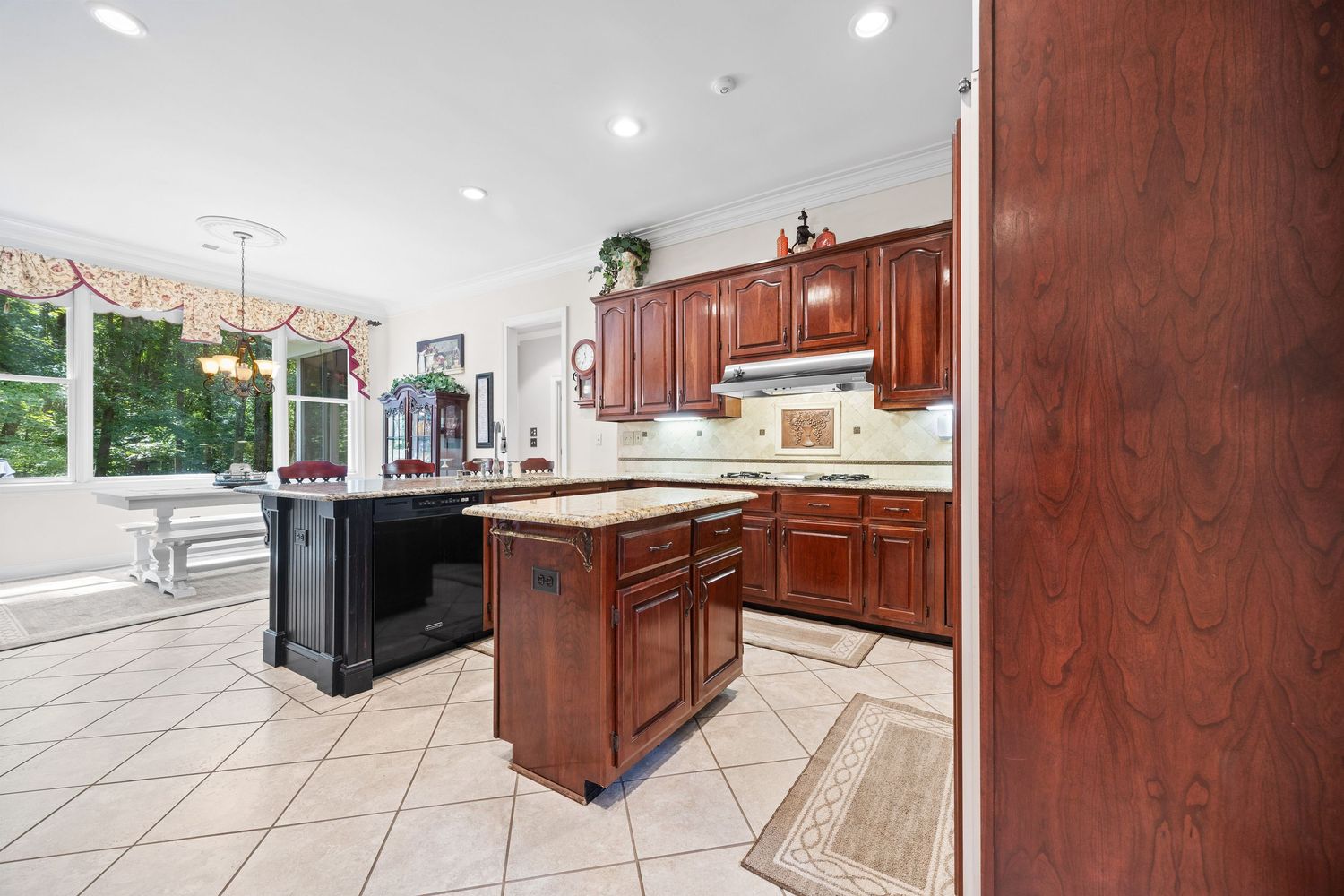 Spacious kitchen with cherry wood cabinets, tile flooring, and black appliances.