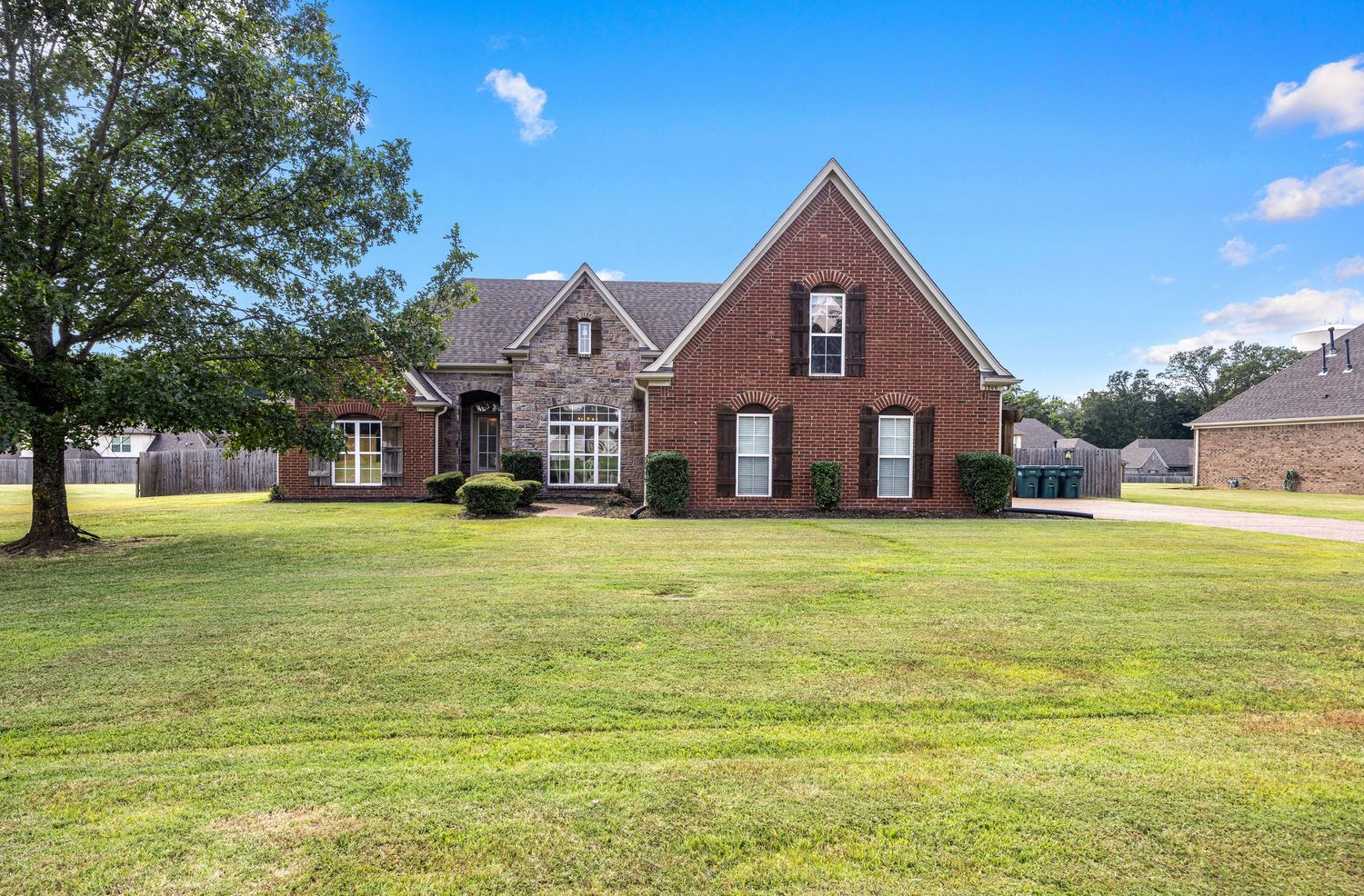 Wide angle view of a large brick estate home with expansive green lawn.