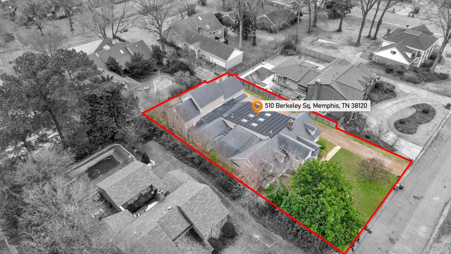 Aerial view of a property boundary outlined in red showing a building and green space with partial black and white effect.