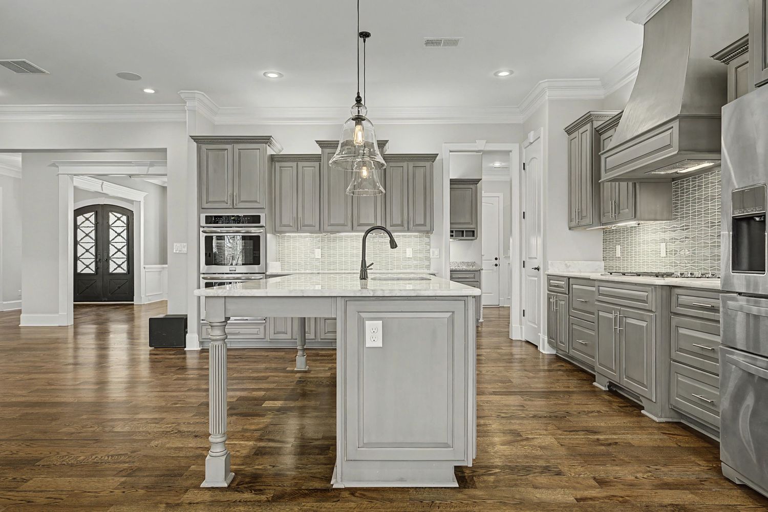 Elegant gray kitchen with hardwood floors features a large center island and custom cabinetry with modern pendant lighting.