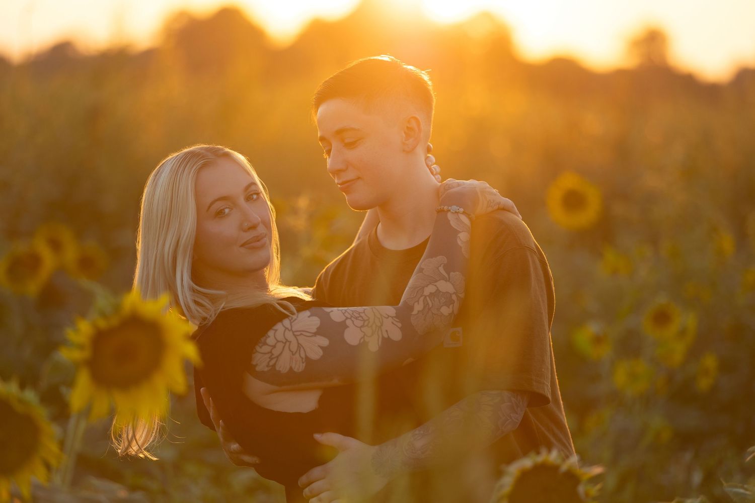Couple enjoying romantic sunset photoshoot in field of bright yellow sunflowers.