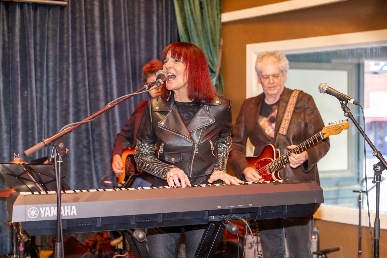 Musicians performing on stage with instruments against a blue curtain backdrop.