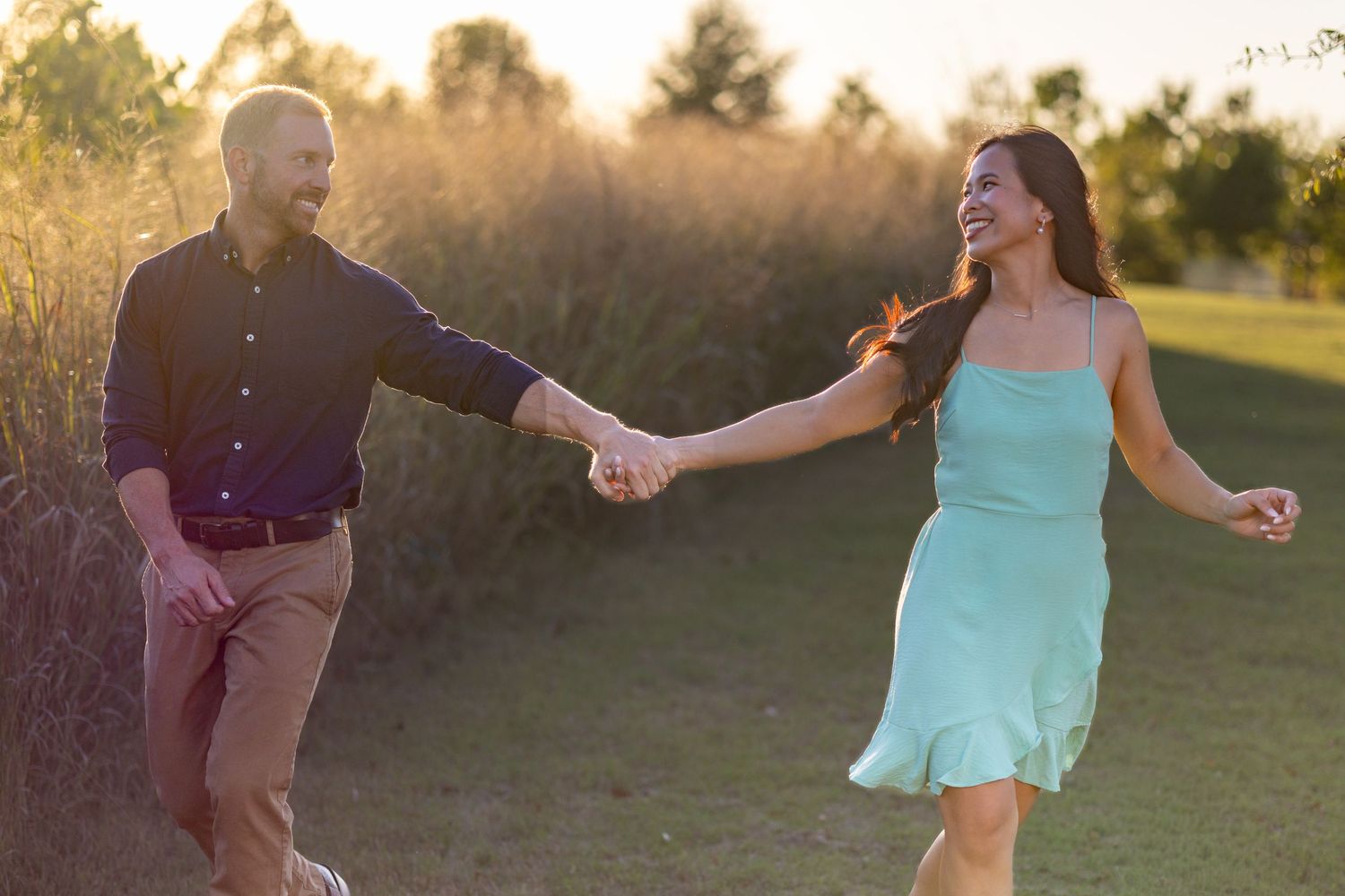 A couple dances and twirls in a field at sunset.