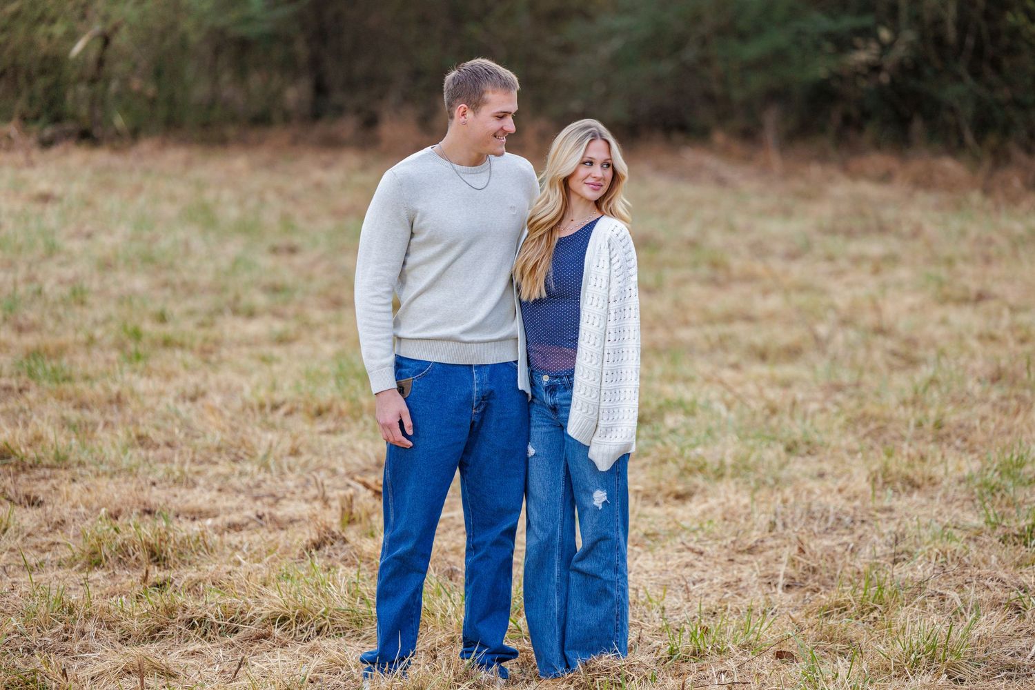 A couple in casual attire shares tender moments together in a grassy field during an autumn photoshoot.