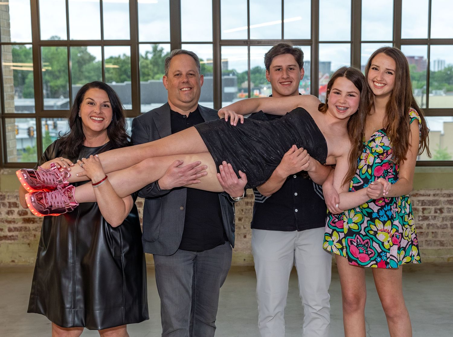 A joyful family of five posing together, with a man carrying a woman while three young adults smile beside them.