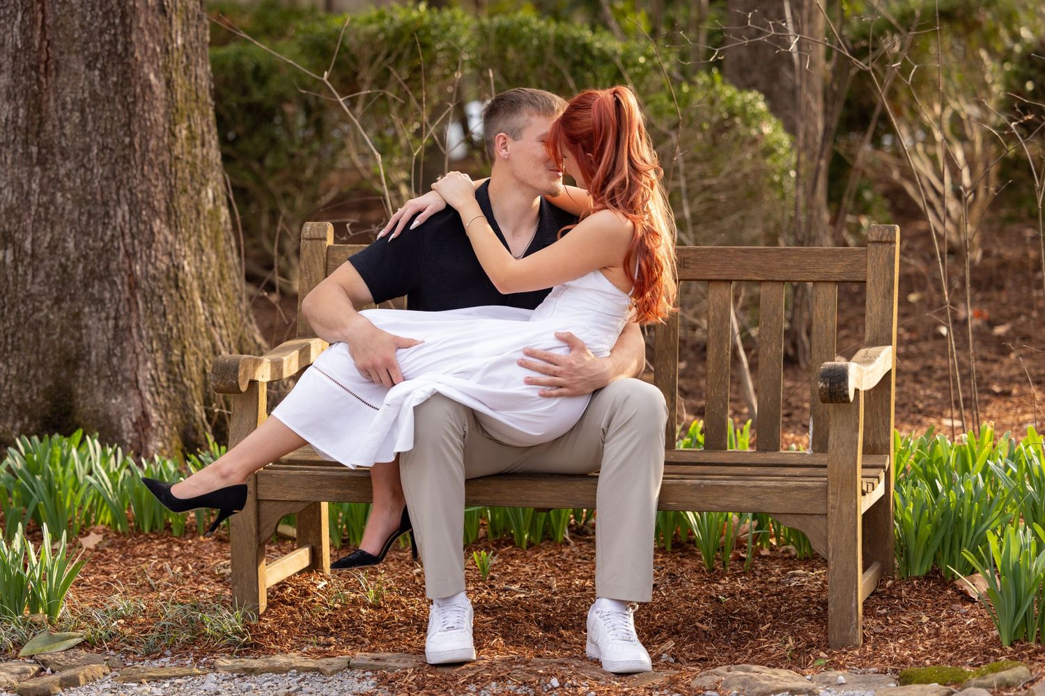 Romantic couple sitting on a wooden bench in a garden with blooming daffodils in the background.
