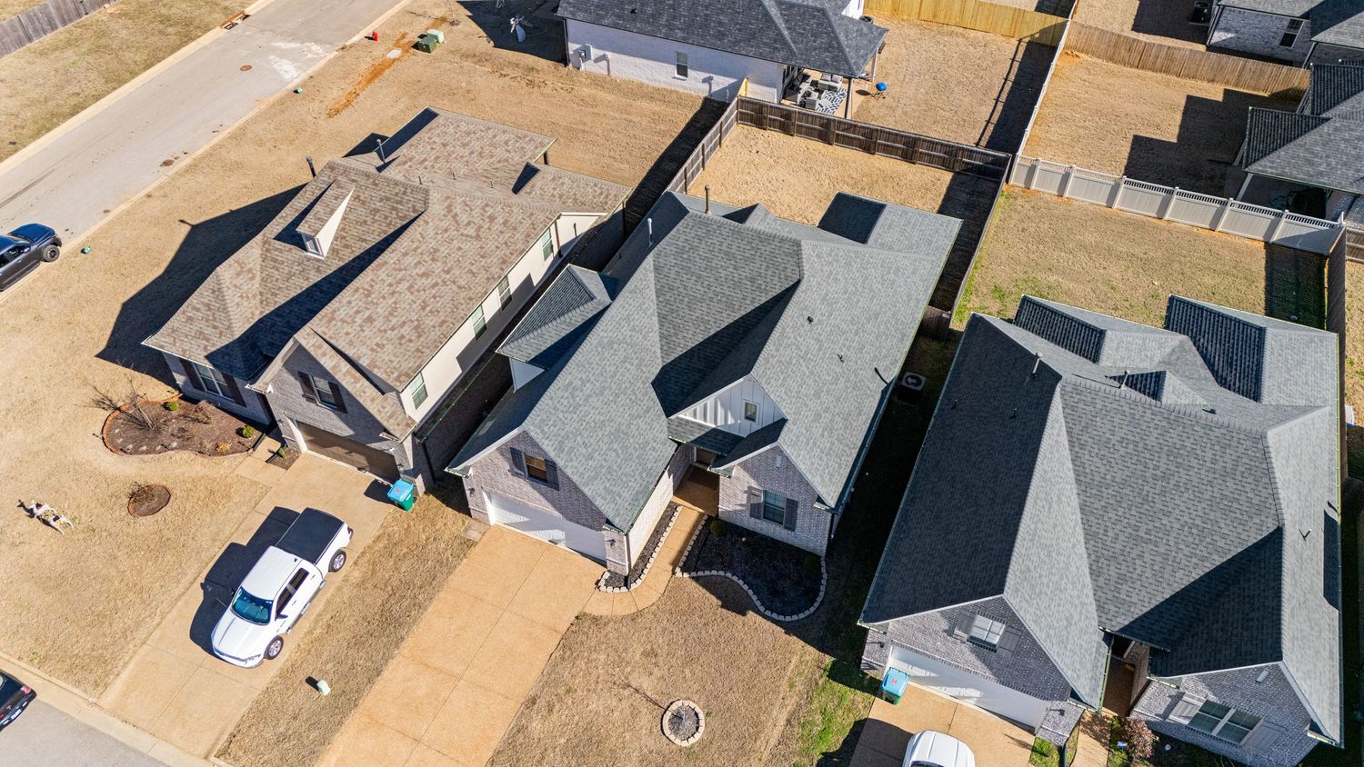 Aerial view of suburban neighborhood with gray rooftops and driveways on a sunny day.