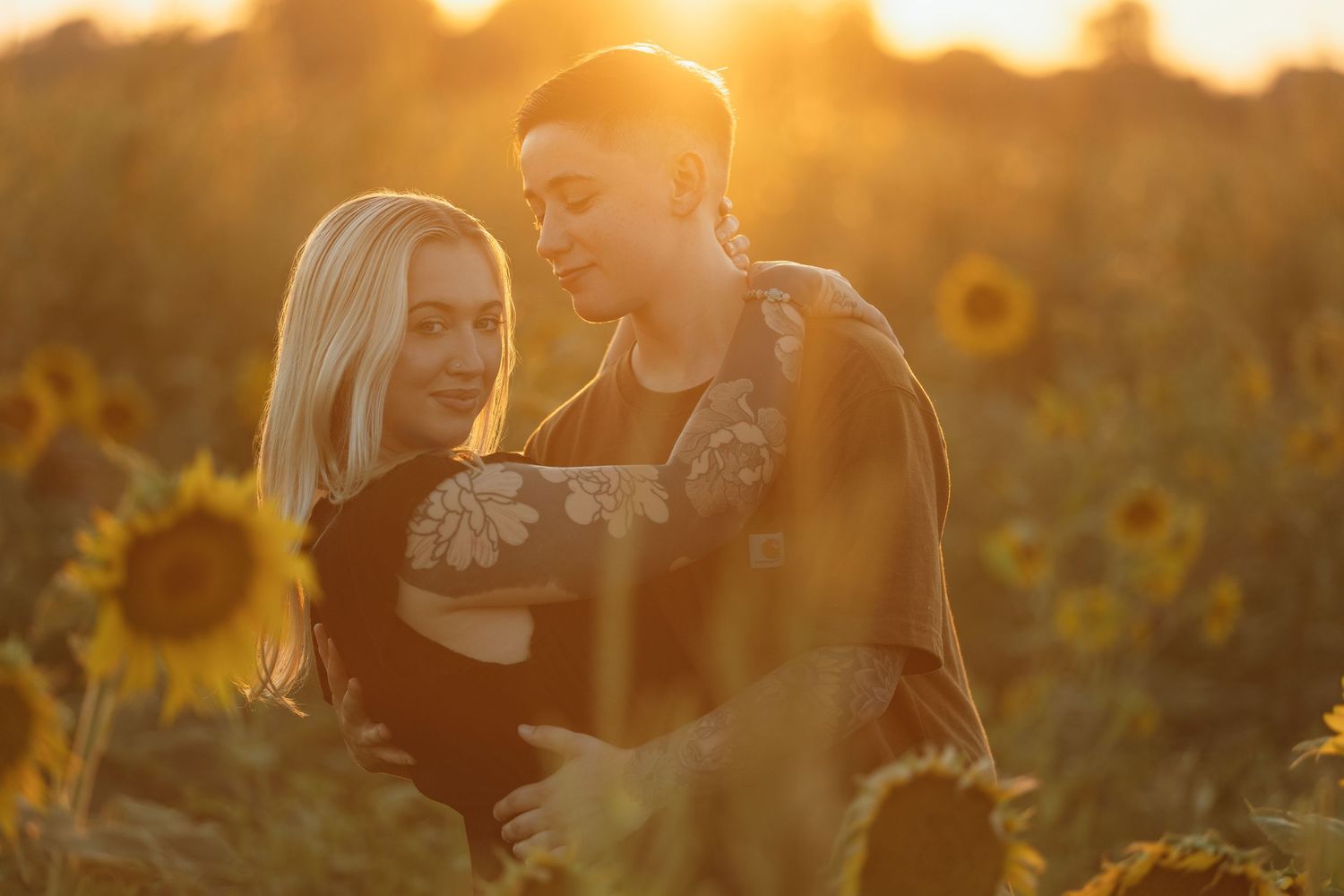 Tender moment between couple in sunflower field bathed in golden sunset light.