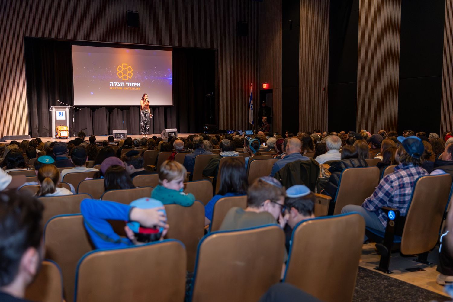 Wide shot of filled auditorium with projection screen during presentation.