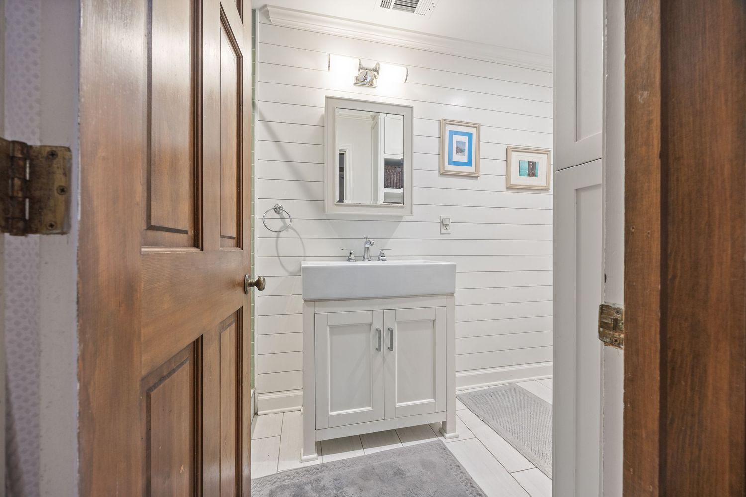 Clean white bathroom with shiplap walls, modern vanity, and wooden door.