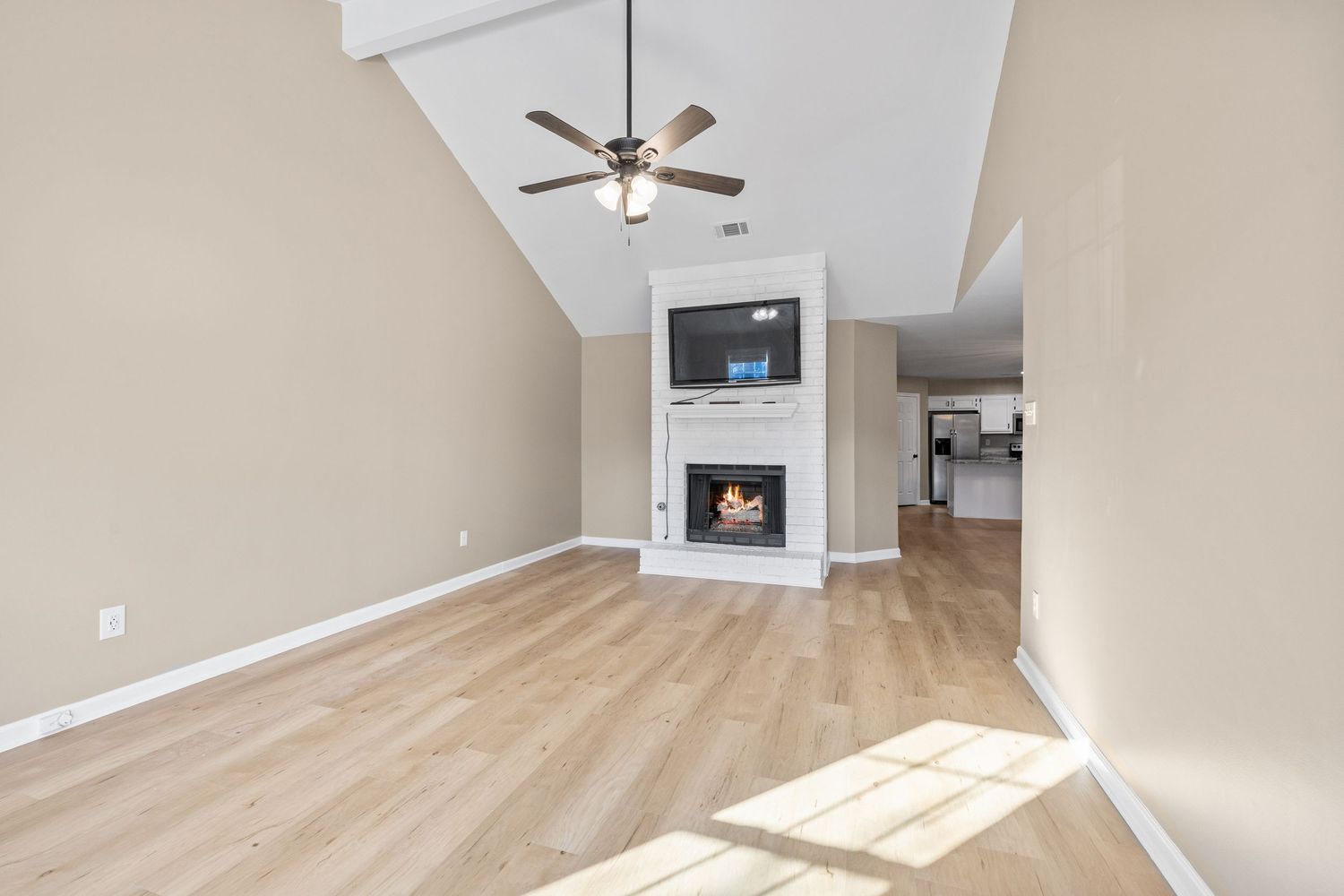 Empty living space with light hardwood floors and beige walls illuminated by natural sunlight.