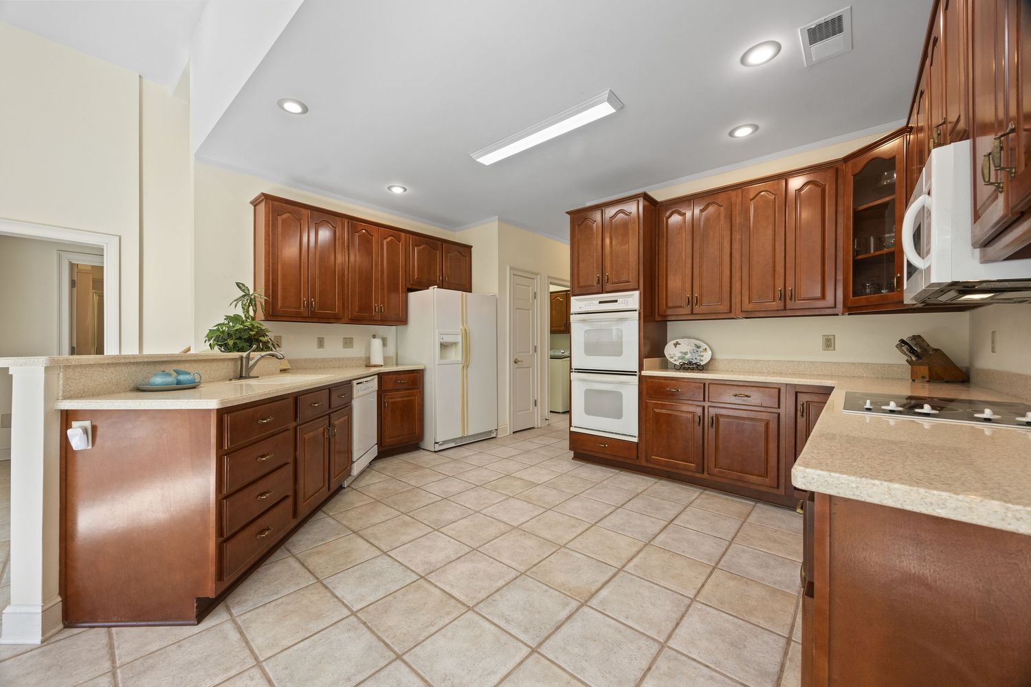 Modern kitchen interior with brown wood cabinets, tile flooring, and recessed lighting.