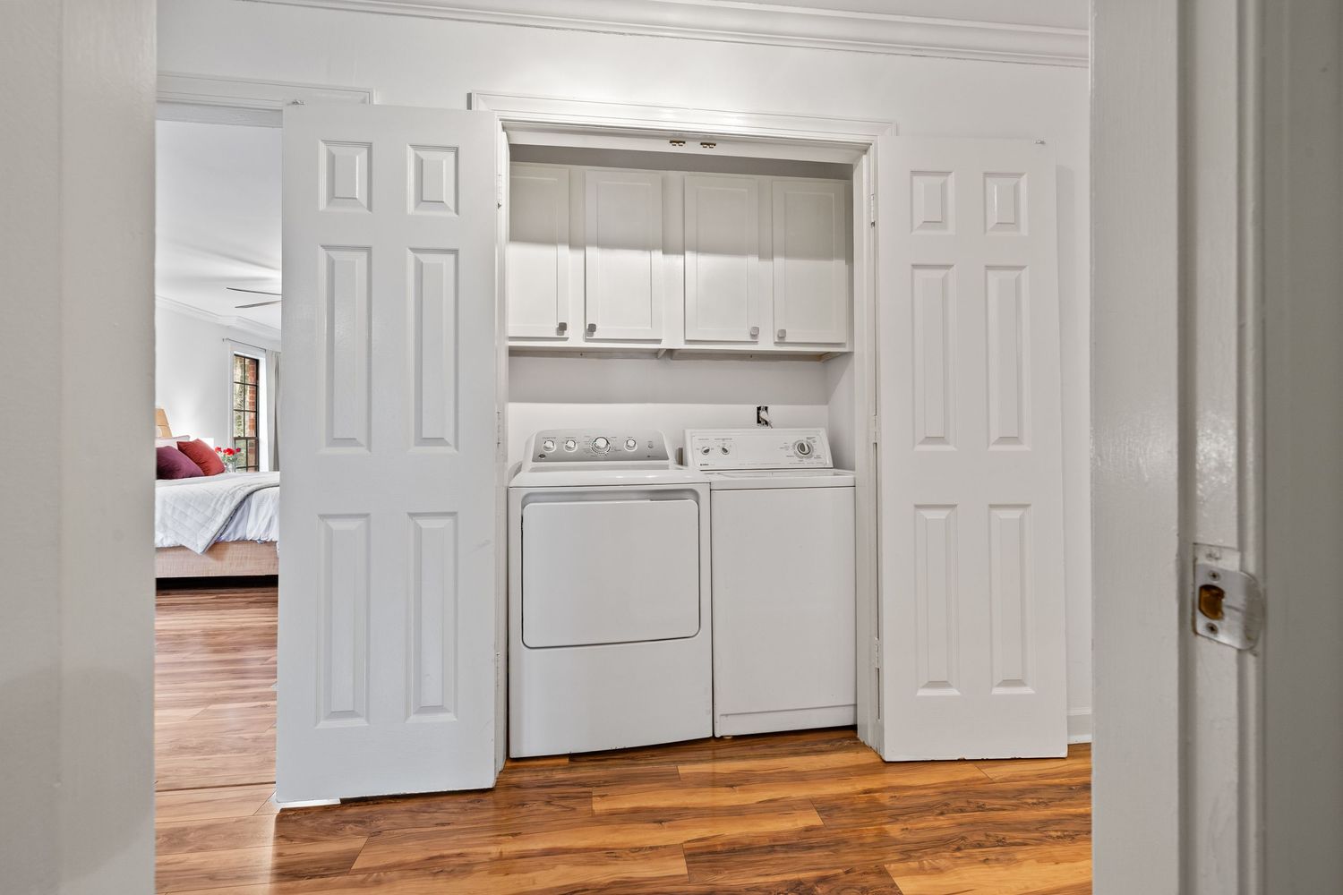 Modern apartment interior with white cabinets, hardwood floors, and multiple doorways leading to different rooms.