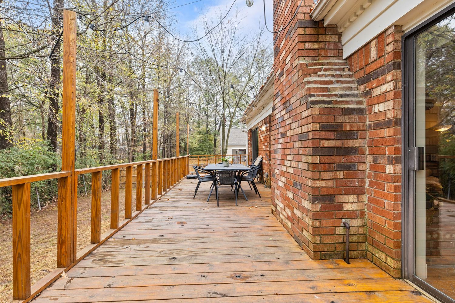 A long wooden deck walkway with brick pillars extends through a wooded area on a sunny day.