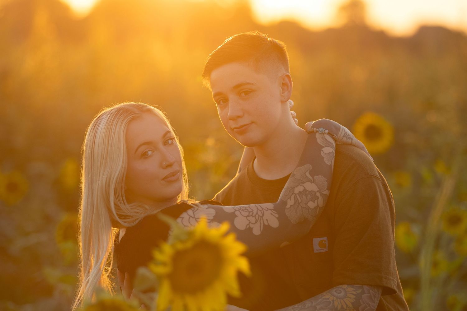 Candid portrait of couple laughing together in sunflower field with warm sunset lighting.