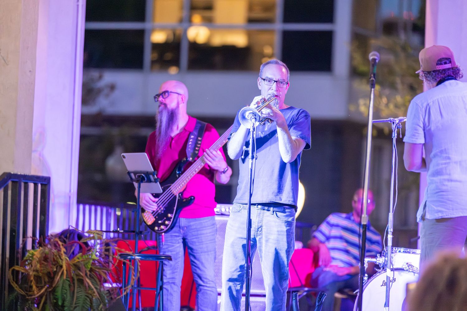Musicians perform on stage with colorful purple lighting and instruments.
