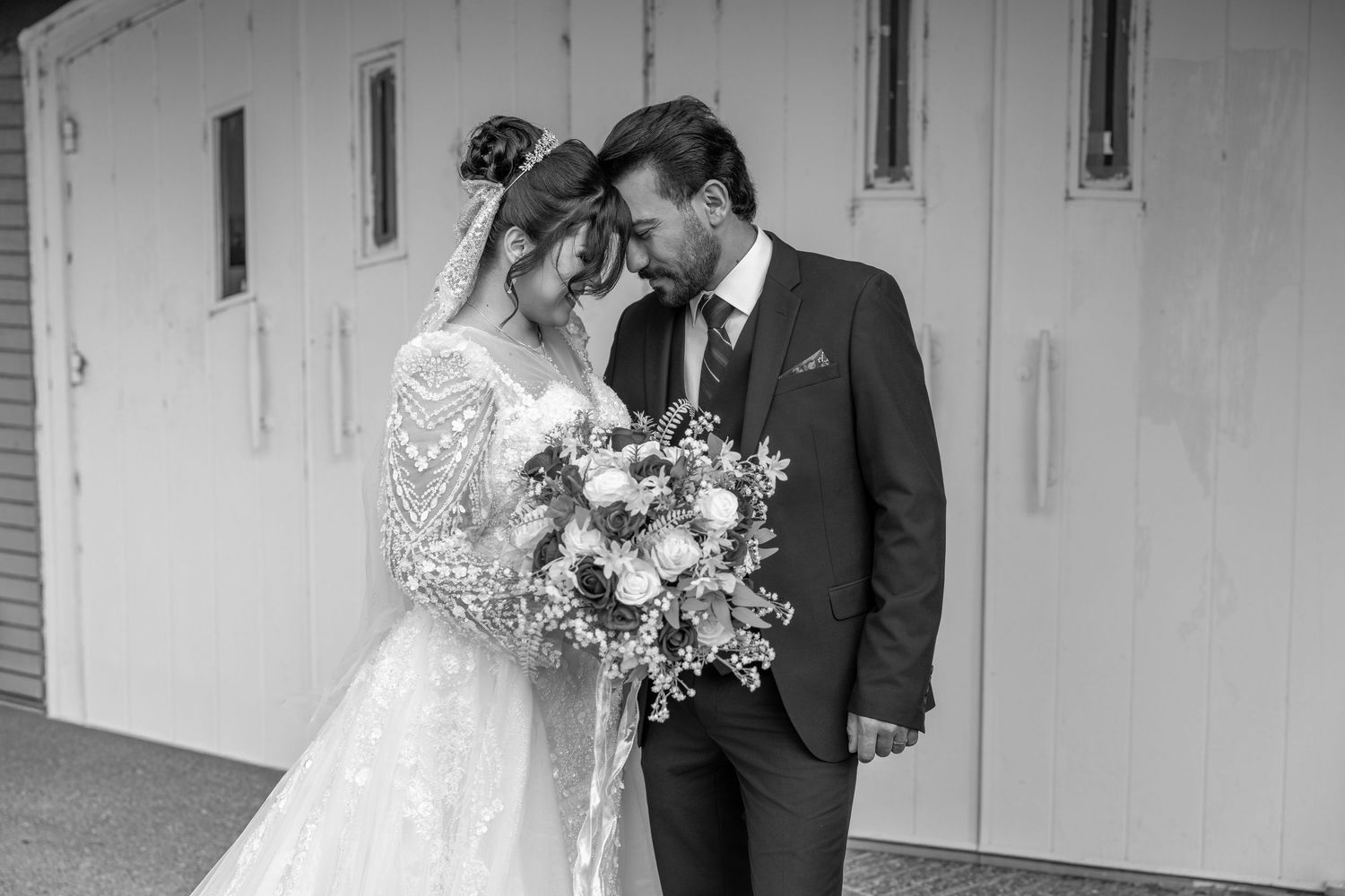 Black and white wedding portrait showing tender moment between couple against white wall.