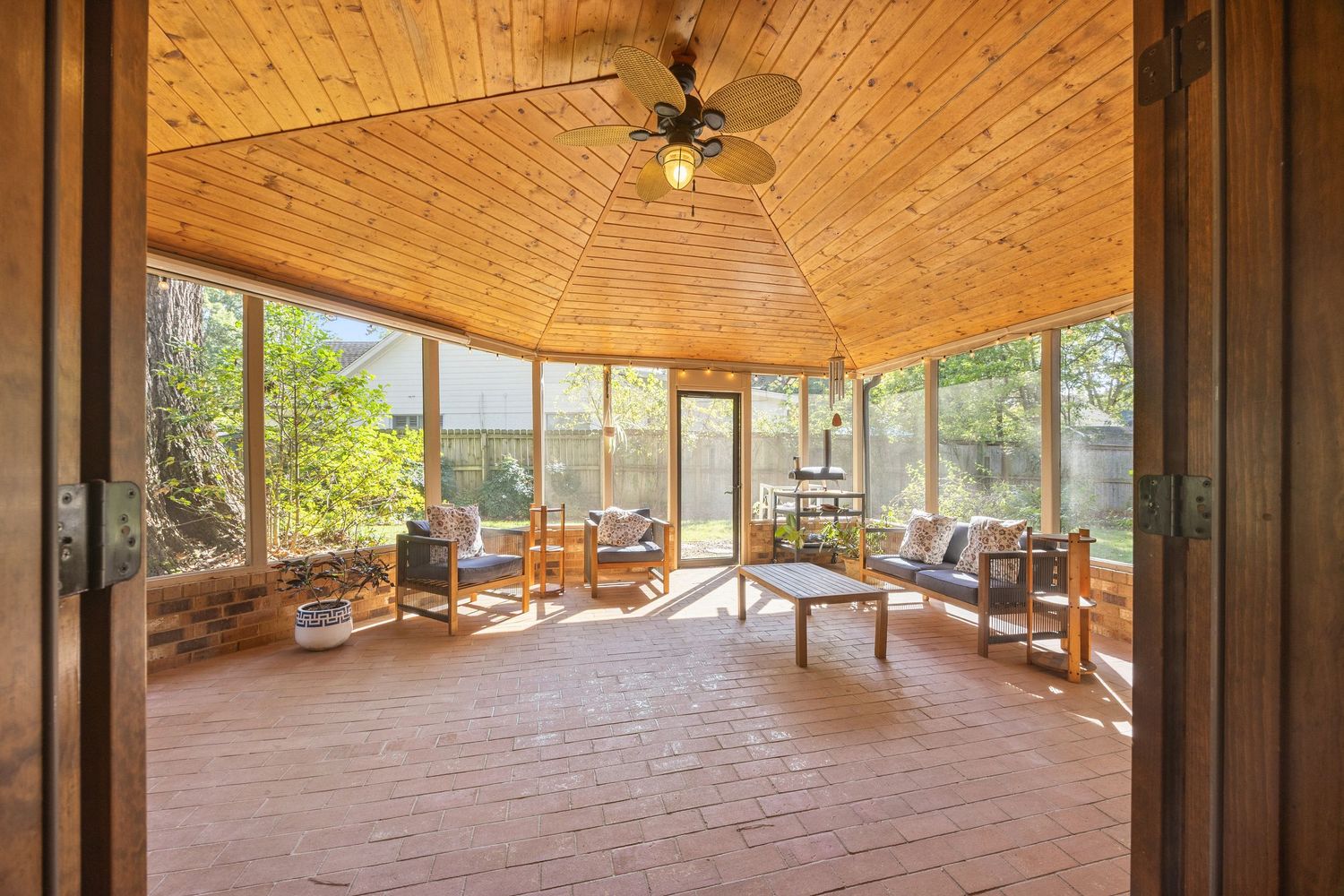 Bright sunroom with wooden ceiling, multiple windows, and comfortable seating overlooking nature.