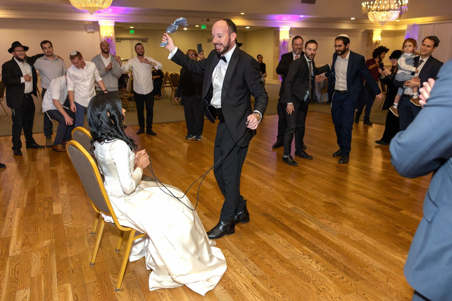 Wedding reception in ballroom with wooden floors and guests dancing.