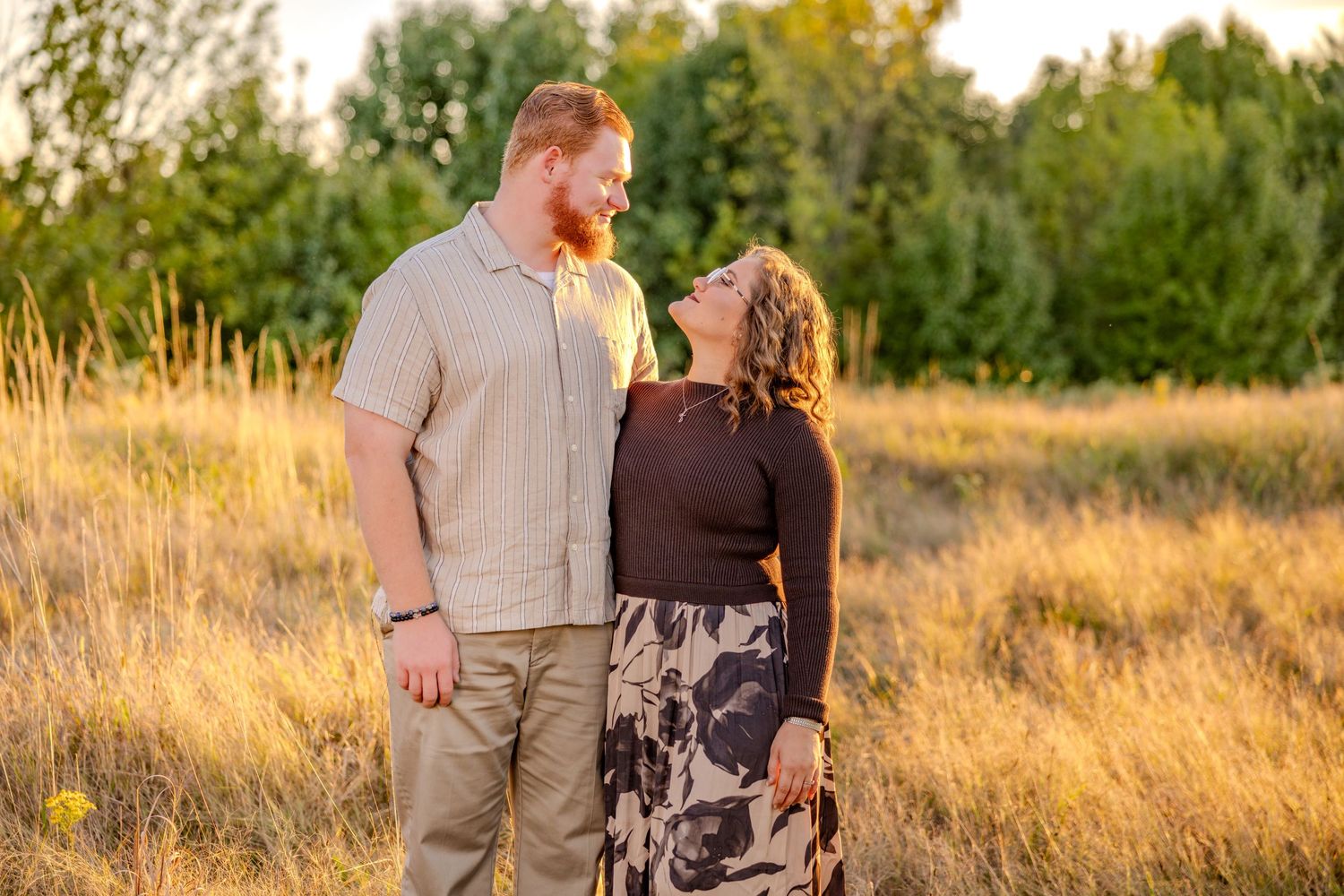 Couple sharing intimate moment in grassy field during golden hour.