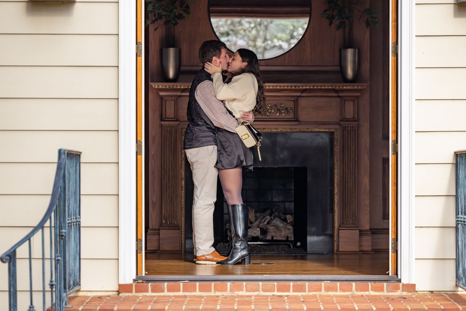 A couple sharing an intimate embrace in the entrance of a home with a wooden door and brick steps.