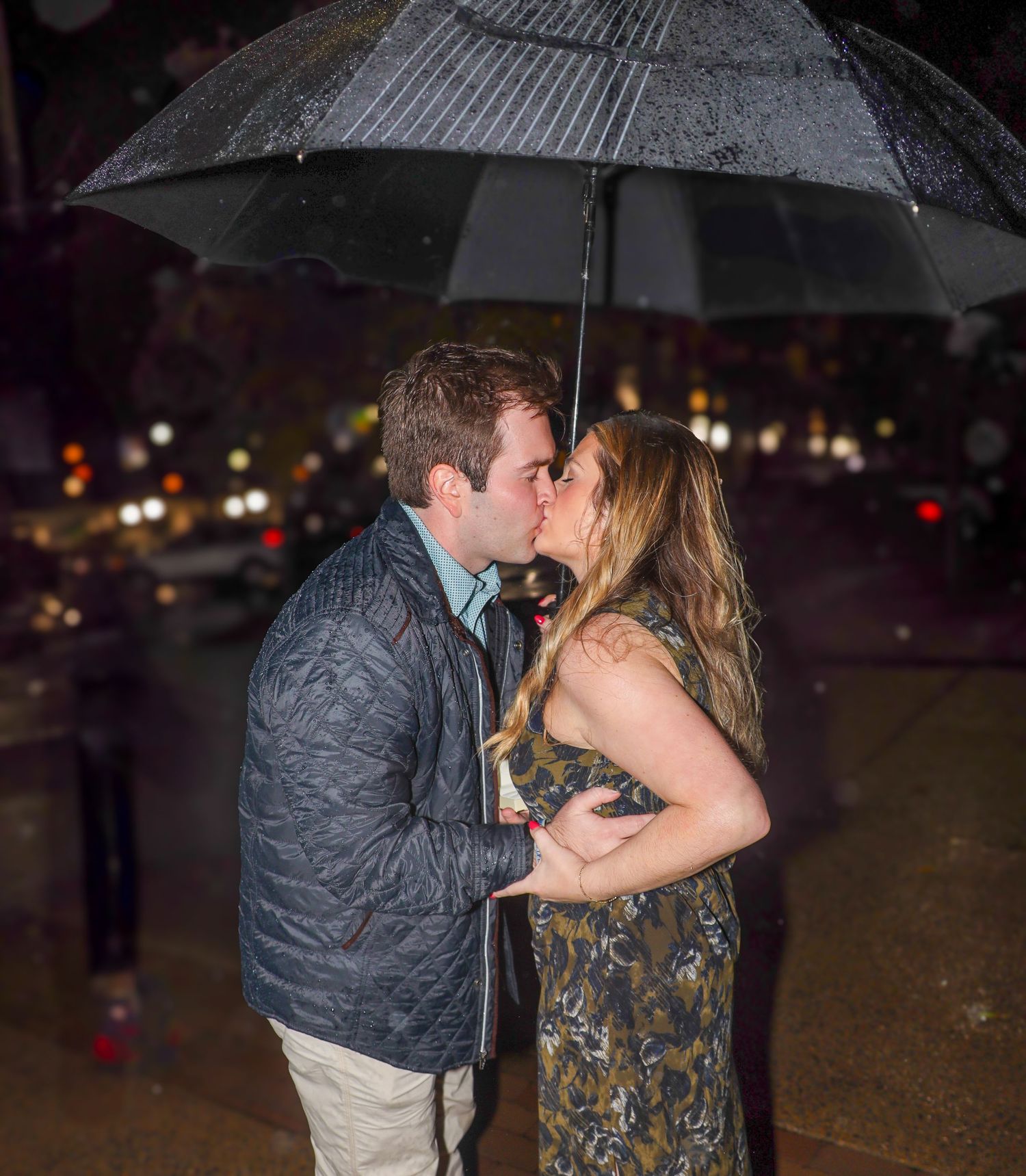 Romantic proposal moment under umbrella at night with city lights in background.