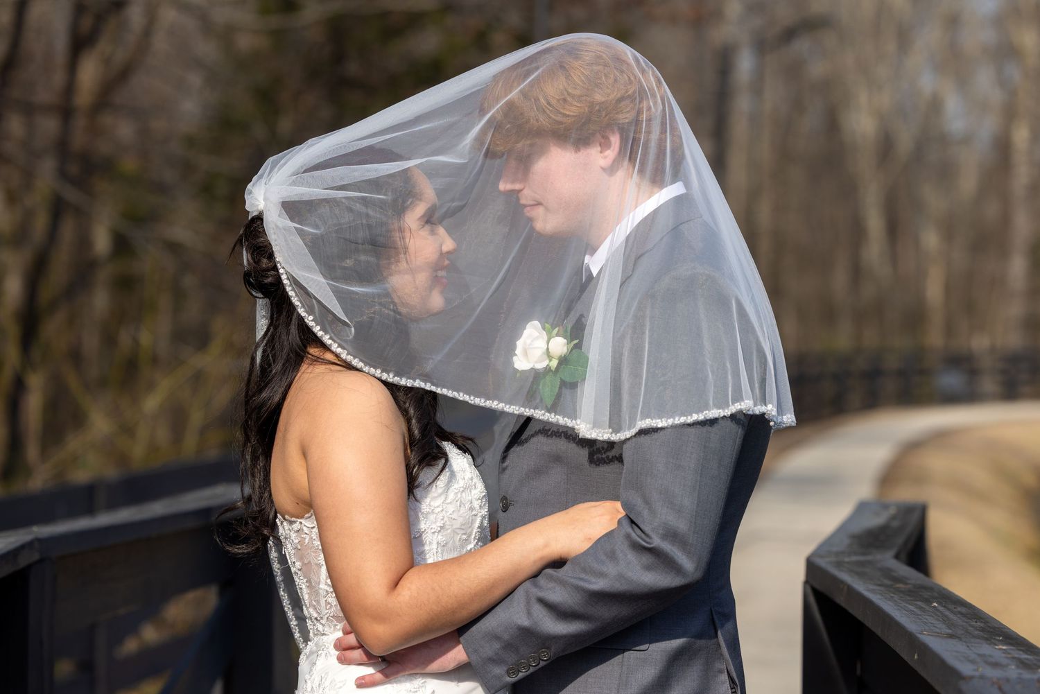 A romantic wedding couple shares an intimate kiss under a flowing veil during their outdoor ceremony.