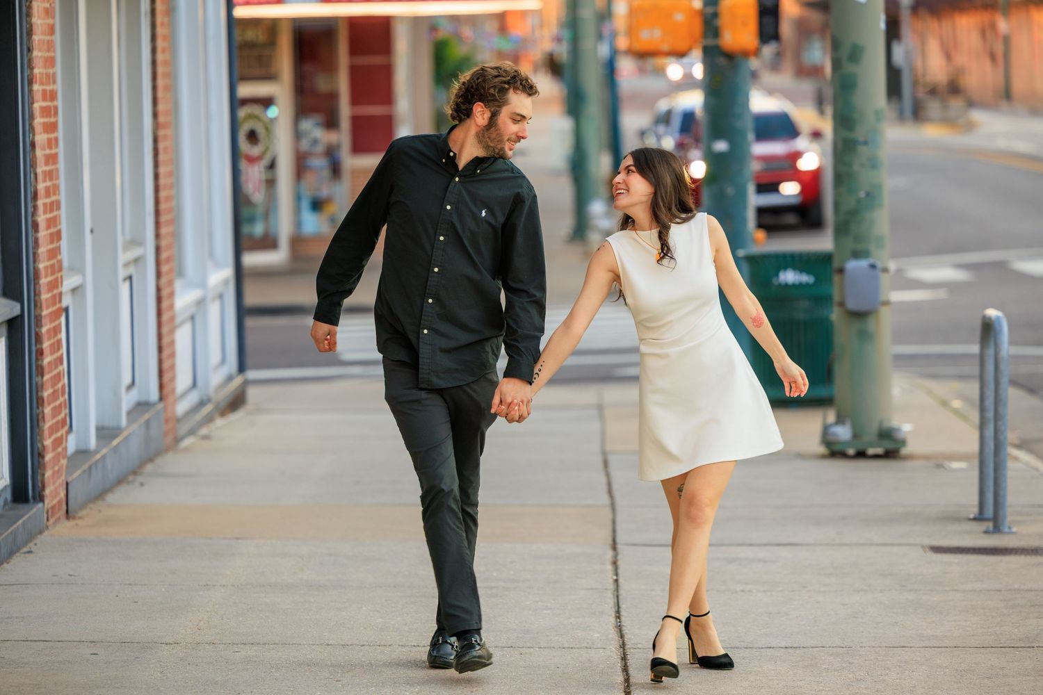 A couple in contrasting black and white outfits hold hands while walking together on a city sidewalk.