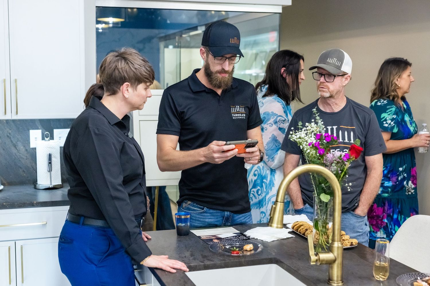 People gathered around a kitchen counter examining food samples at an indoor home design showroom event.