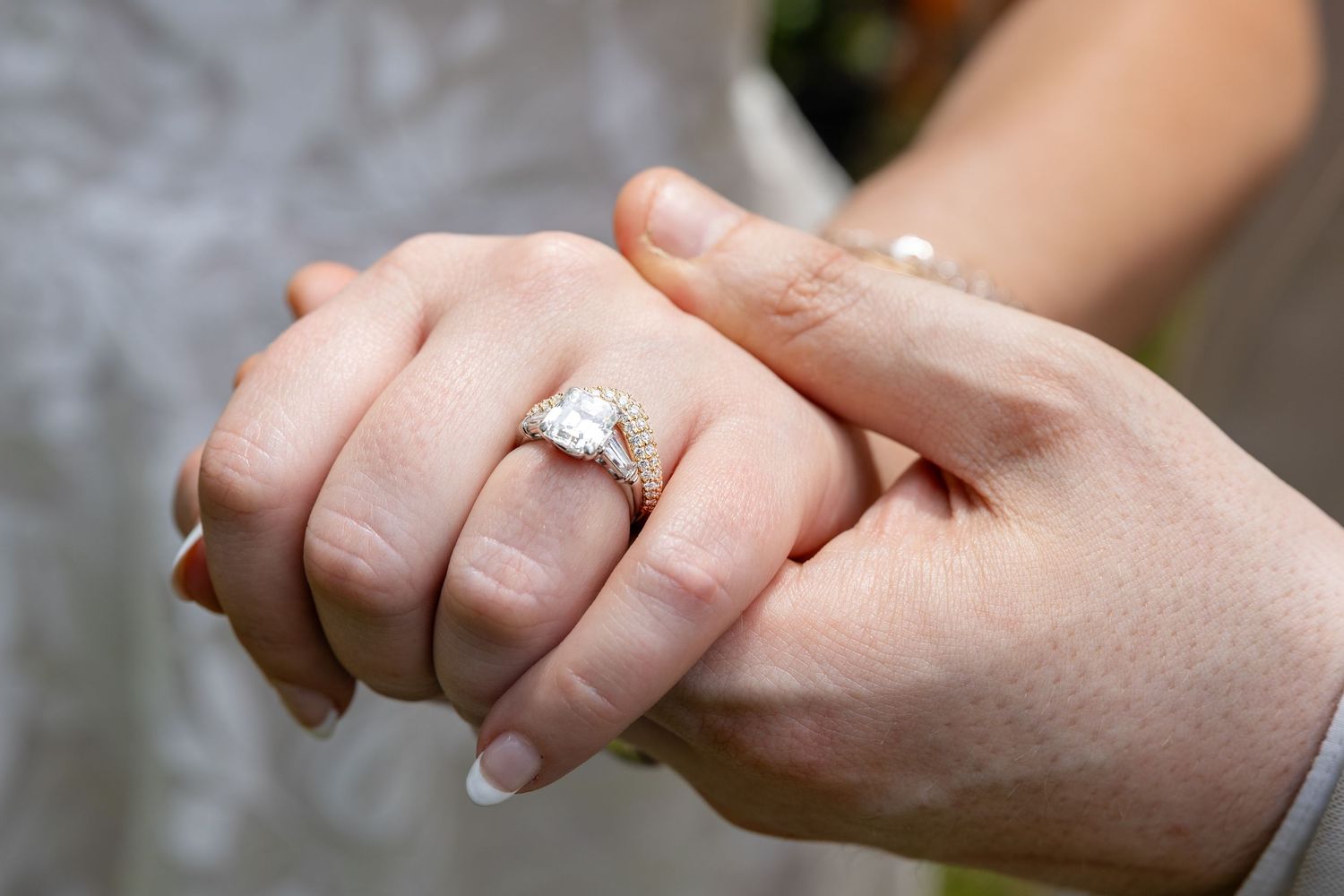 Close-up of a diamond engagement ring on a bride's finger as her partner holds her hand.