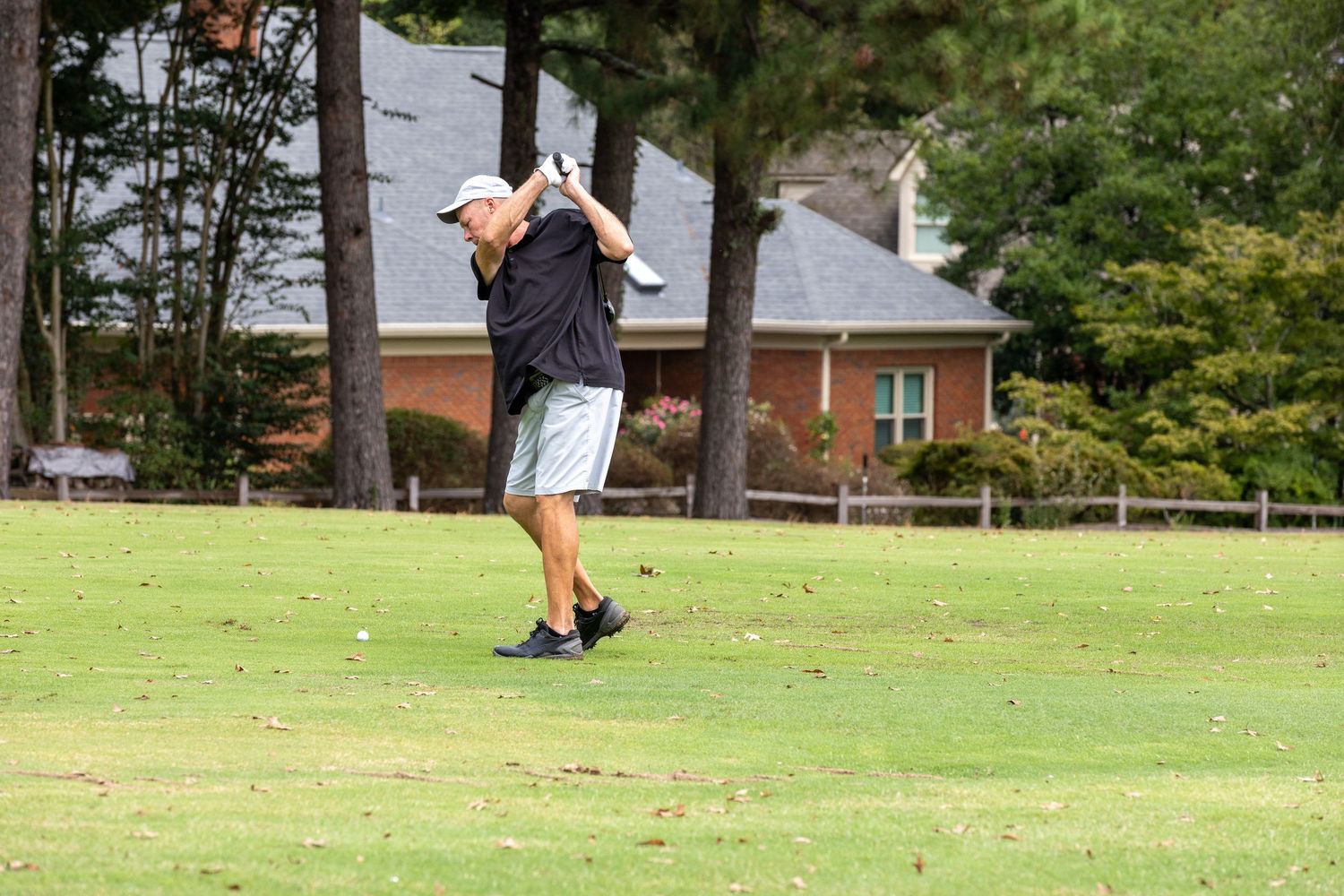 Golfers playing on a sunny day at a lush green golf course with golf carts visible in the background.