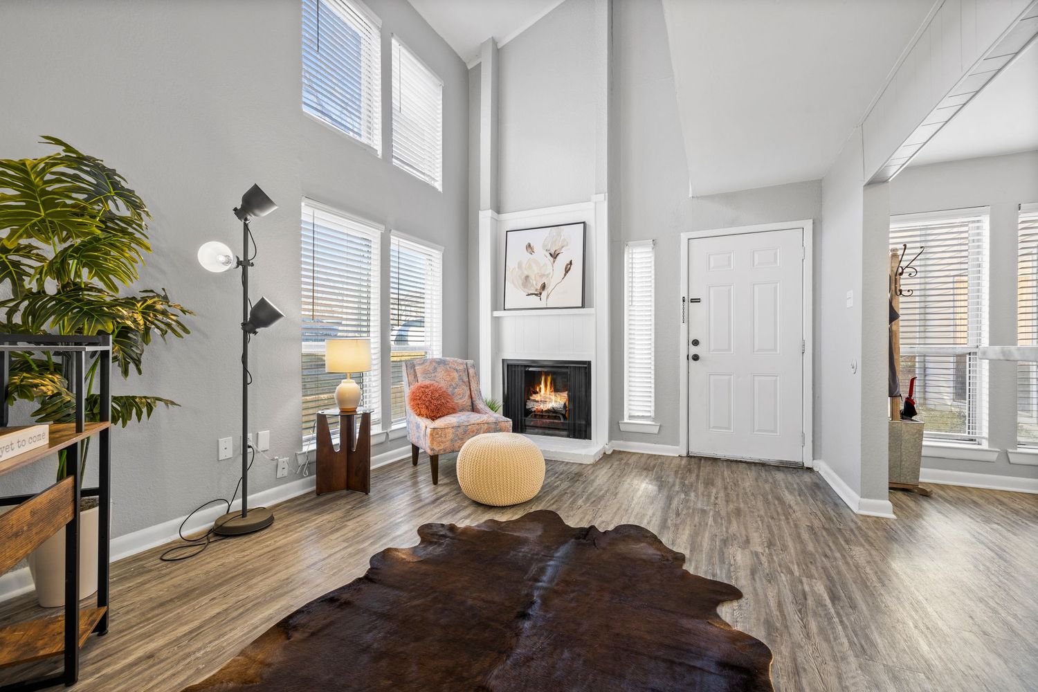 Modern open concept living space with gray wood-look flooring, white walls, and large windows providing natural light.