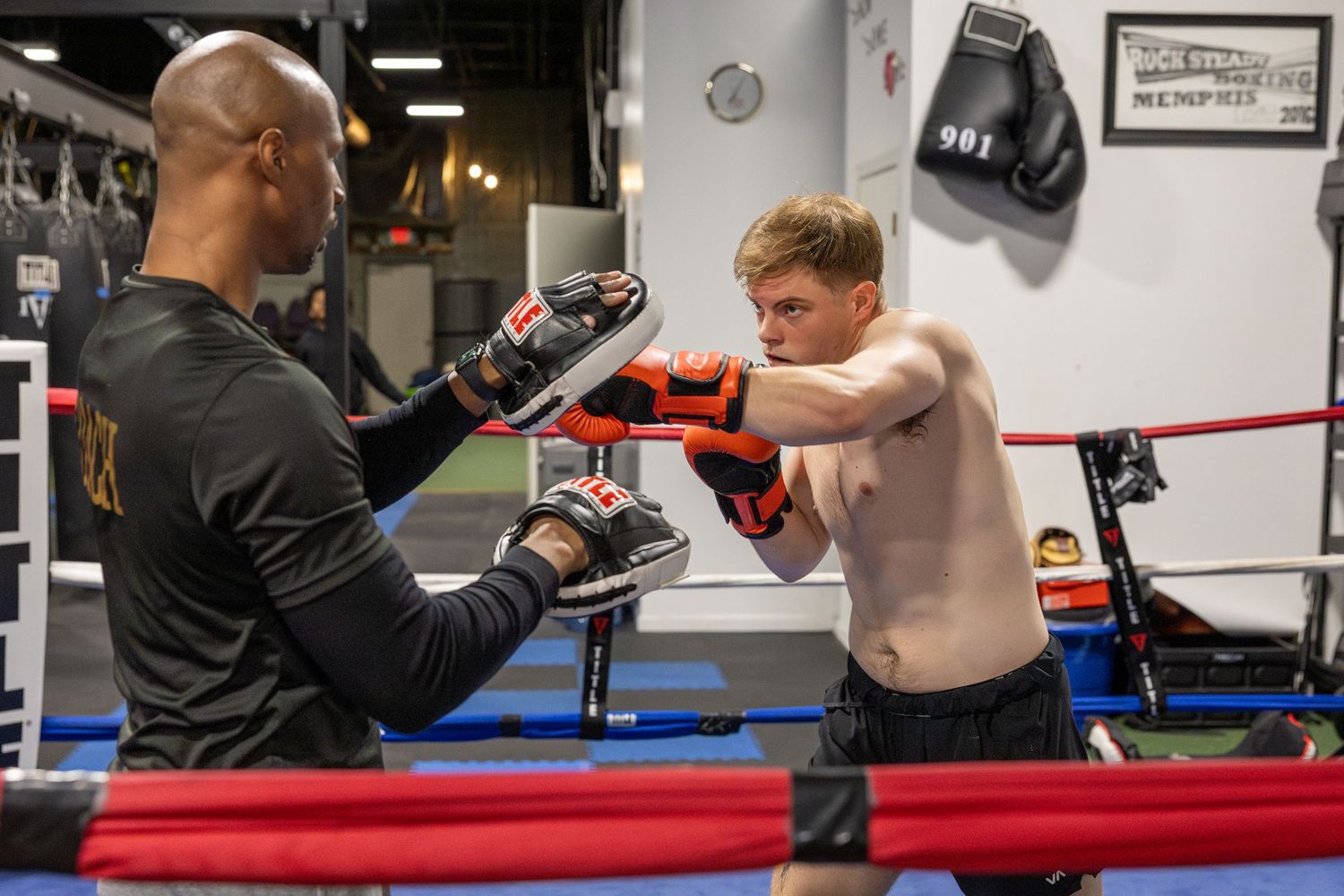 Sparring session in a boxing gym with red and blue ropes.