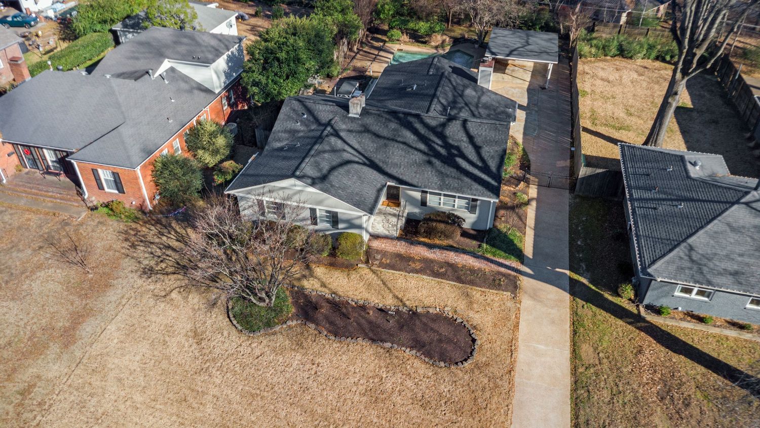 Aerial view of residential homes with dark roofs and dry grass yards in a suburban neighborhood.
