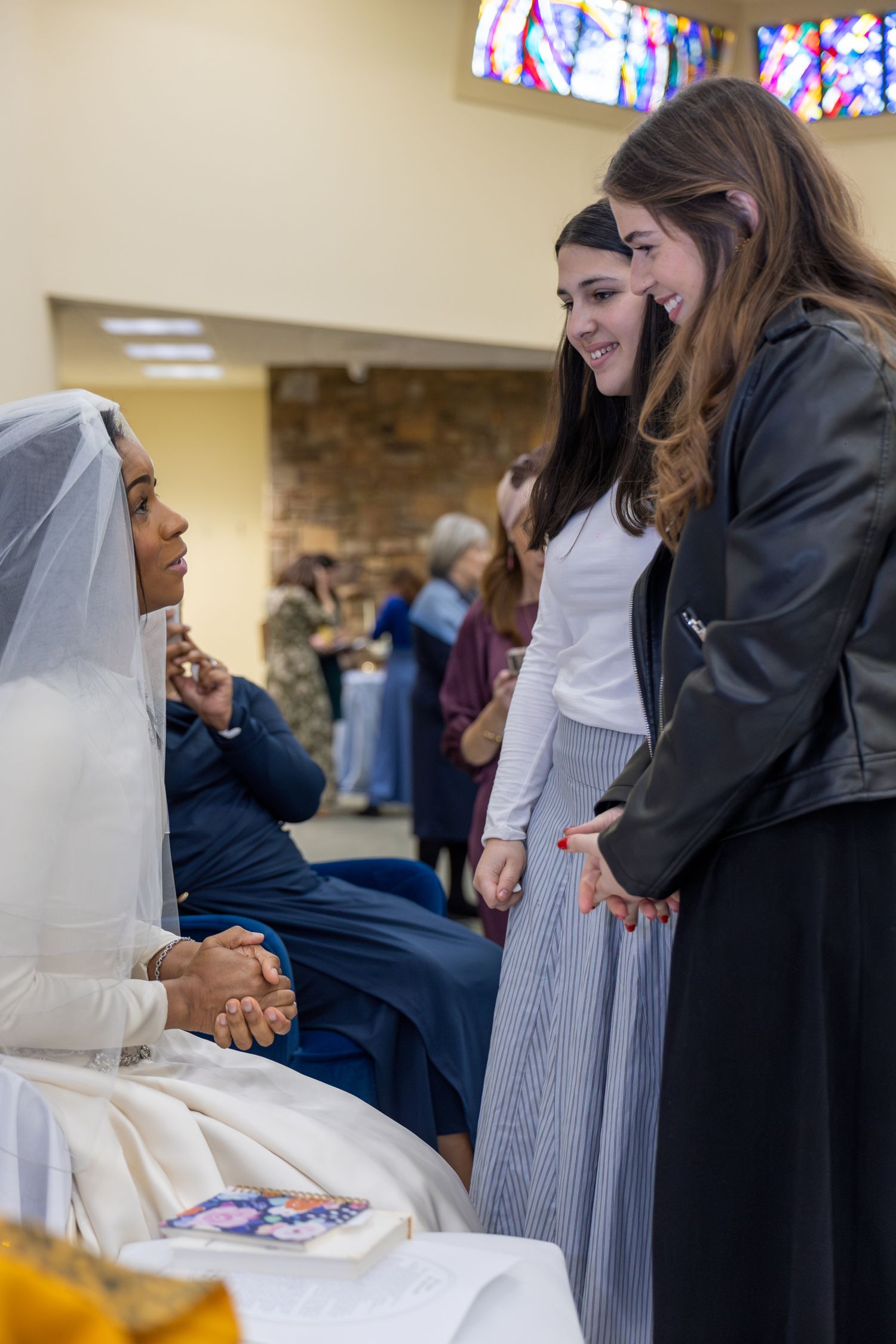 Wedding guests gather inside church with stained glass windows visible in background.