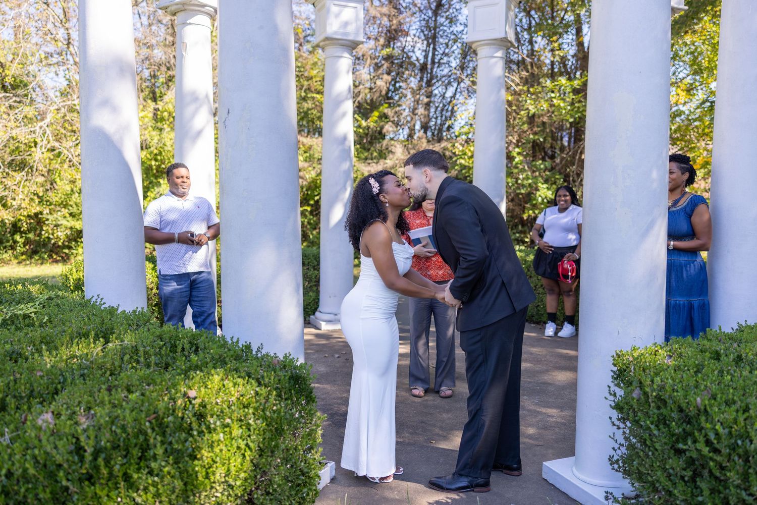 Outdoor wedding ceremony with white columned backdrop and natural landscaping.