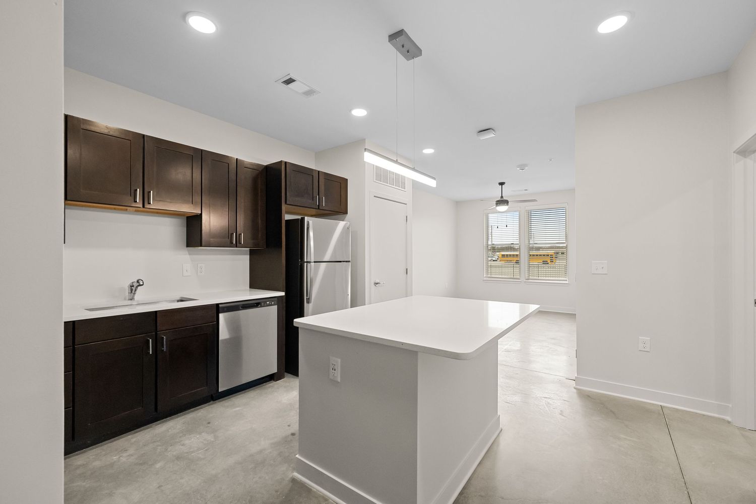 Contemporary open-concept apartment interior with recessed lighting and dark kitchen cabinets.