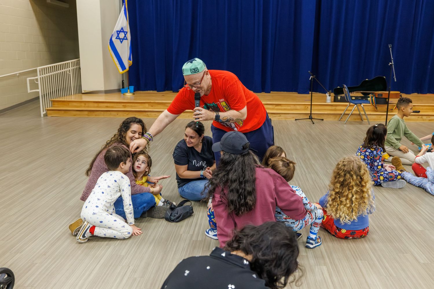 Students participate in interactive learning activities on the gymnasium floor with blue curtains in background.
