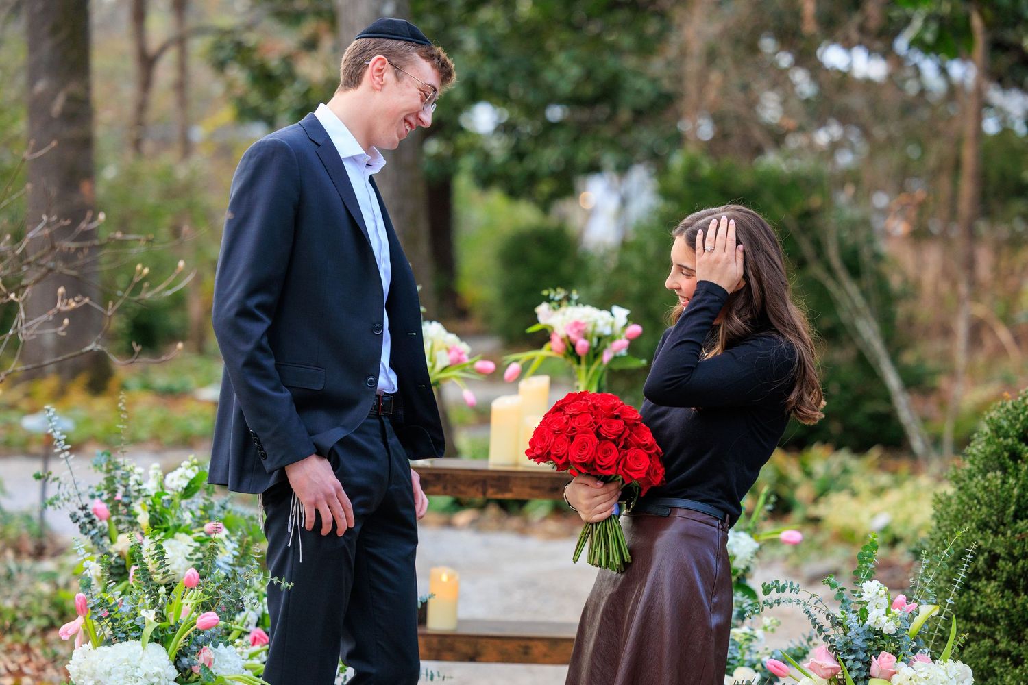 Two people share a romantic moment in a garden setting with red and white flower bouquets.