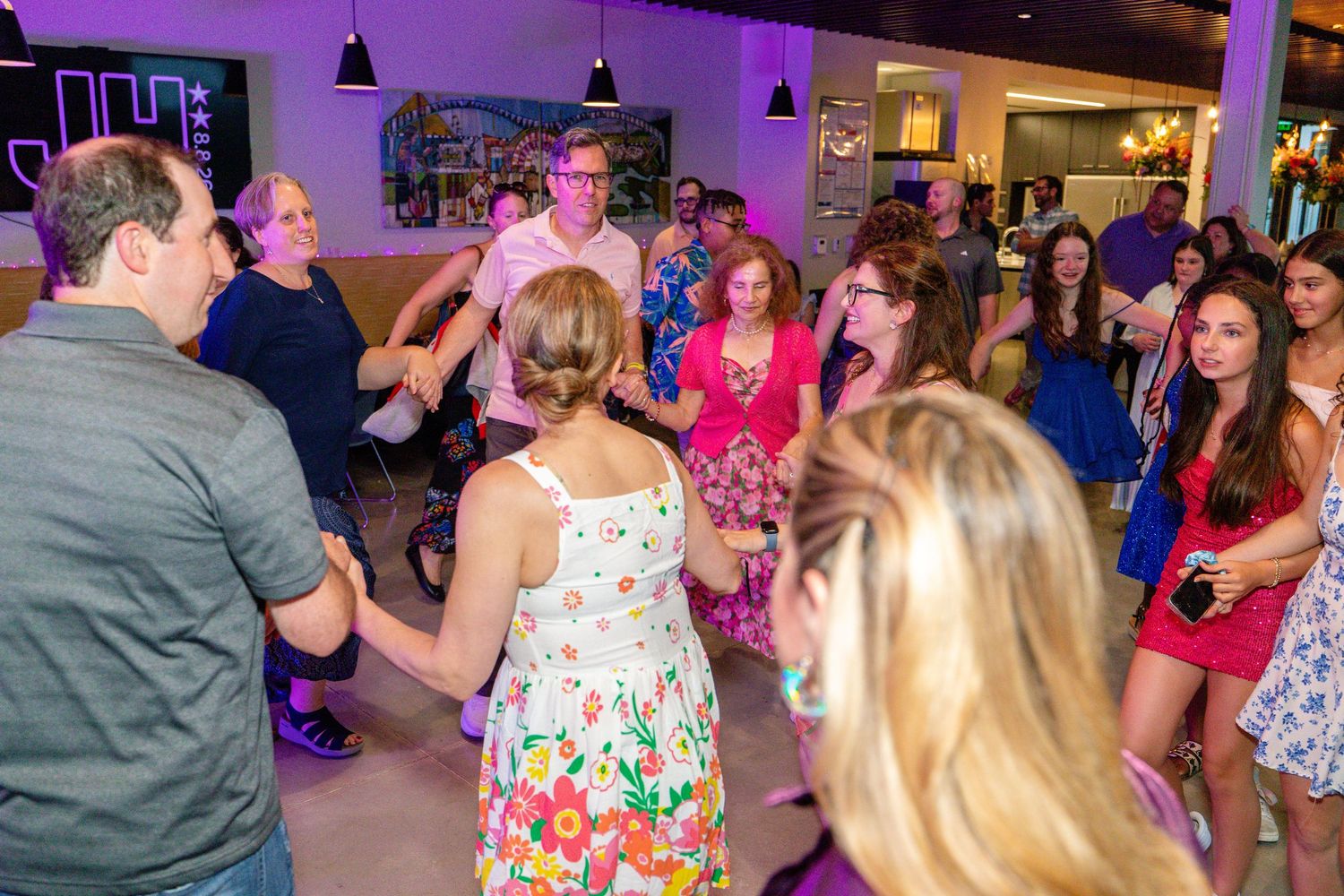 Guests dancing together in a circle at a lively indoor party with purple lighting.