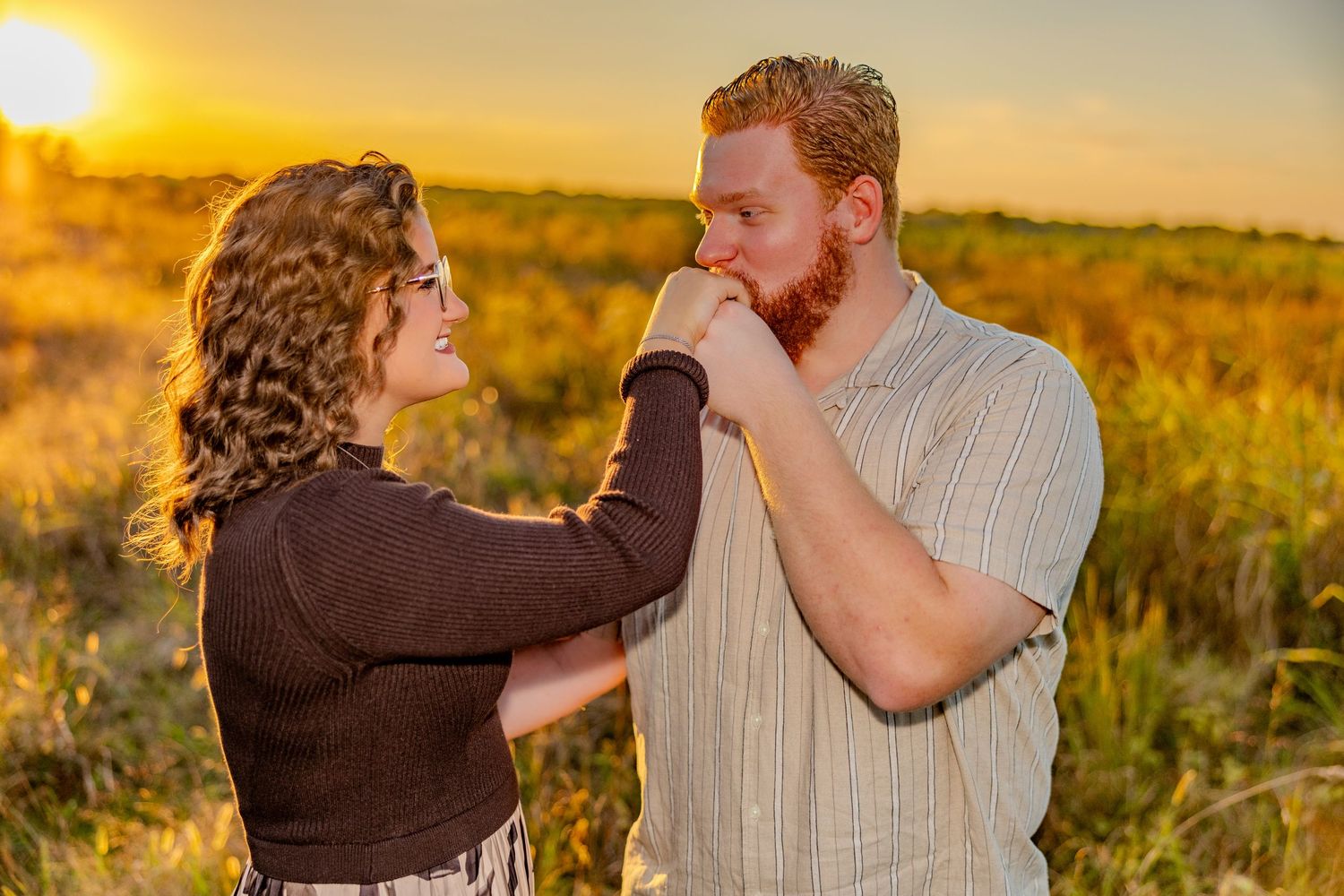 Couple dancing and laughing together in sunlit field at dusk.