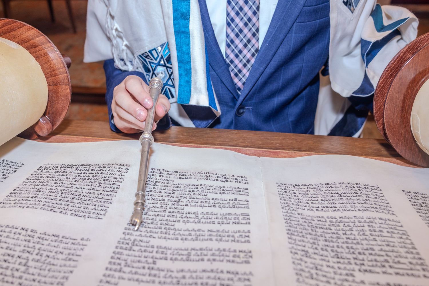 Bar Mitzvah boy reading Torah scroll with a yad pointer during Jewish coming-of-age ceremony.