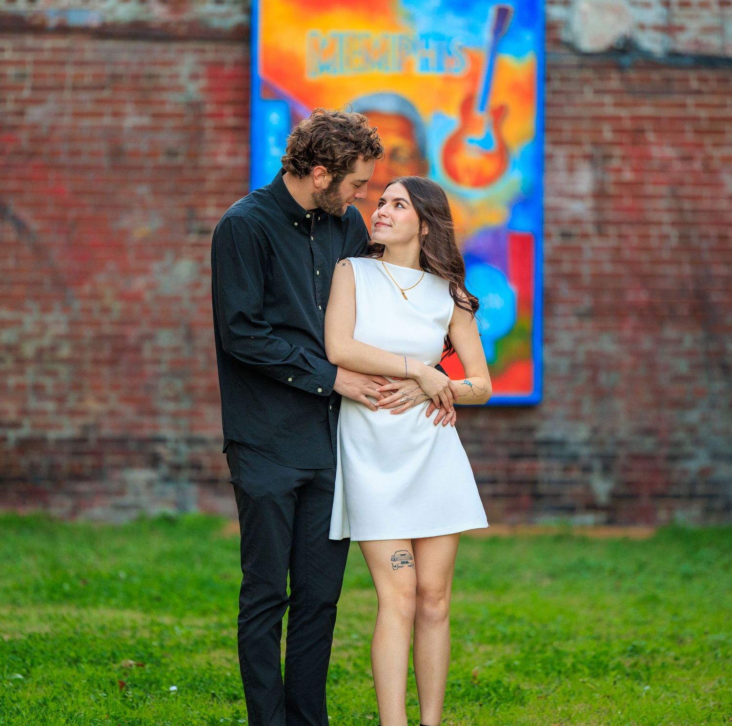A couple shares an intimate moment against a colorful graffiti wall and green grass background.