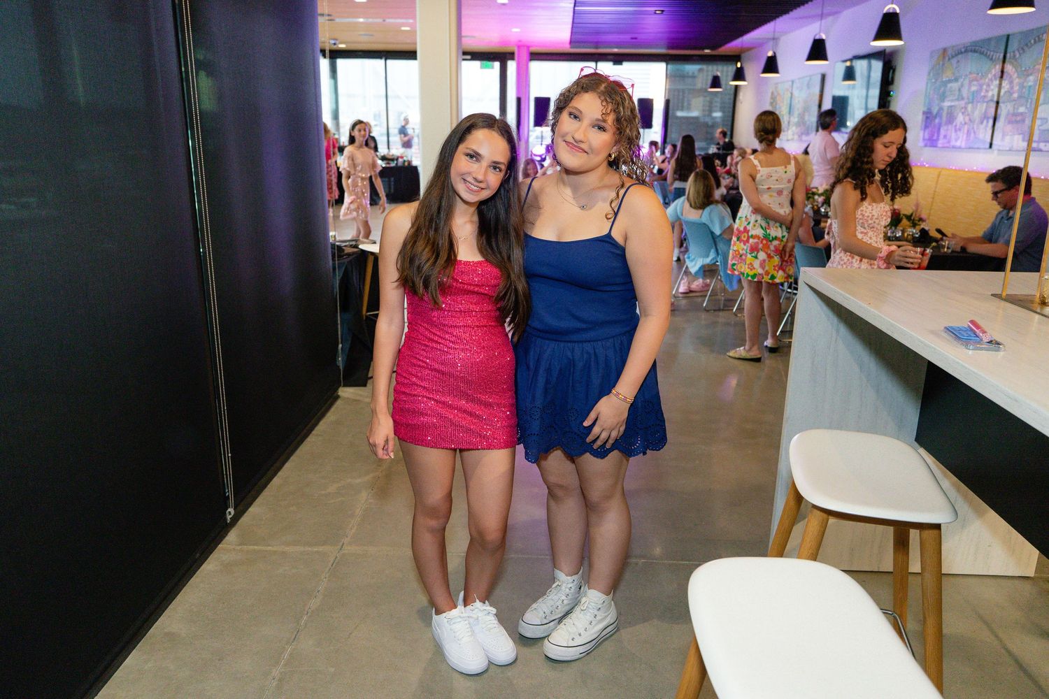 Two girls in colorful dresses posing together at an indoor party venue.