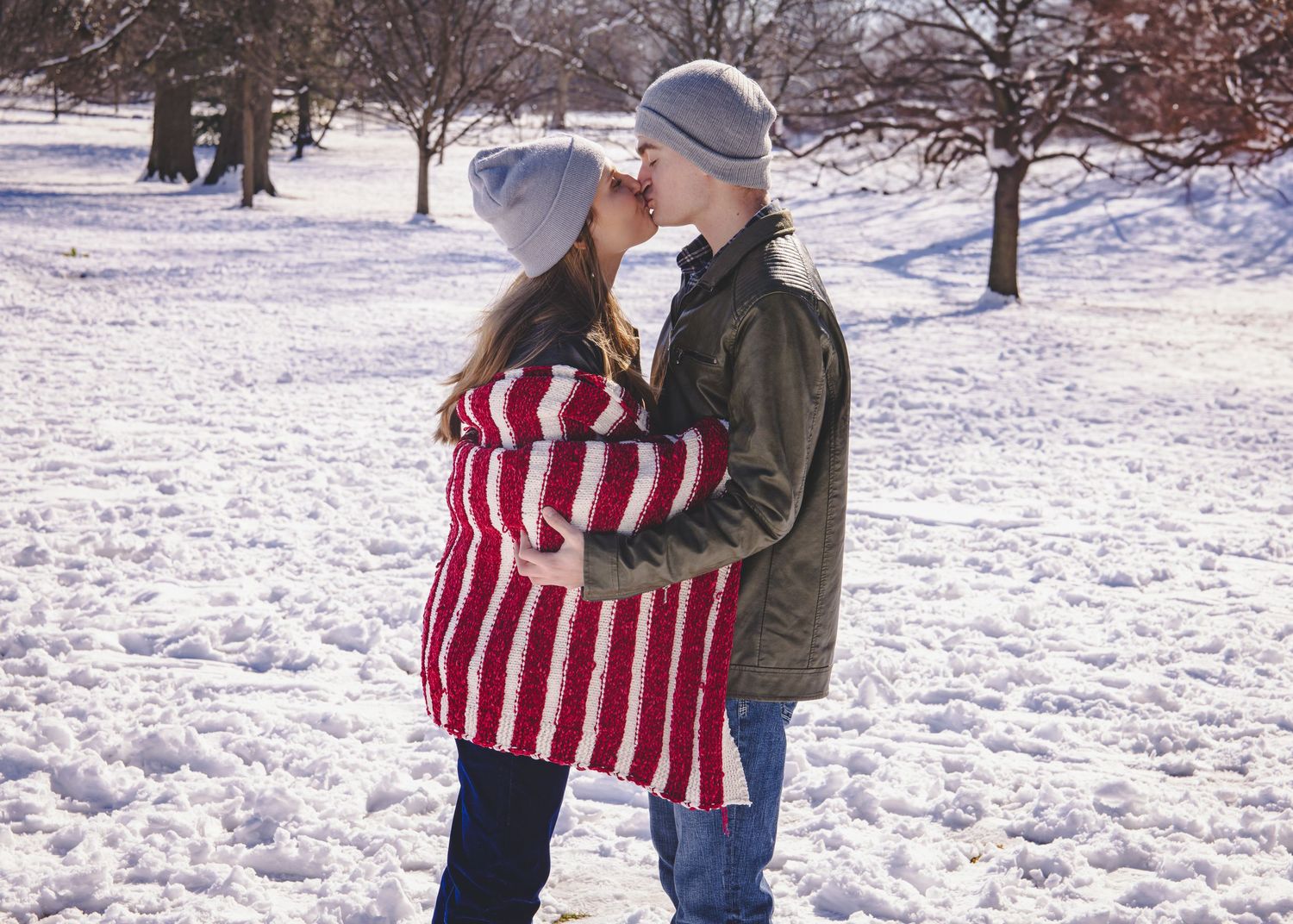 A couple shares a romantic moment in a snowy winter landscape wearing warm clothing.