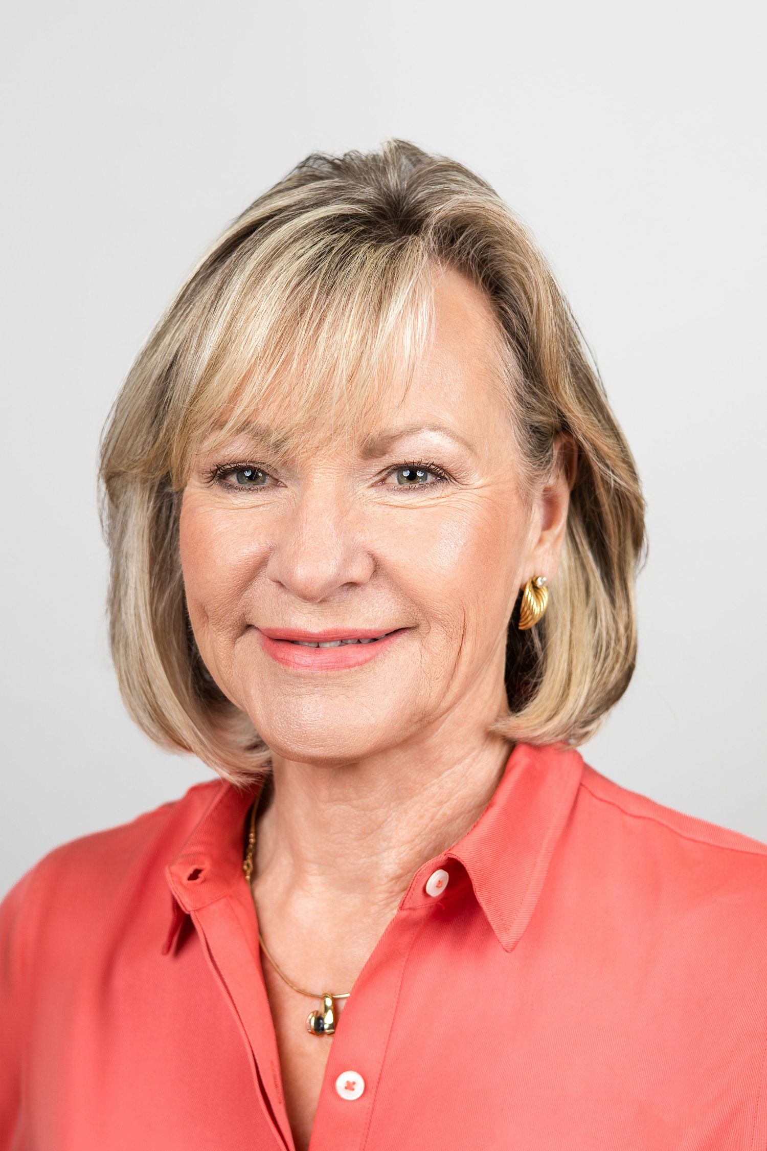 Professional headshot portrait of someone wearing a coral colored blazer against white background.