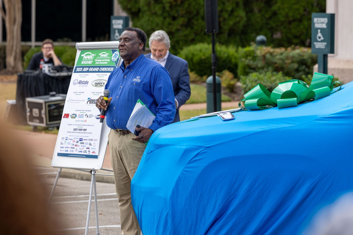 Professional outdoor gathering with display boards and signage visible in the background.