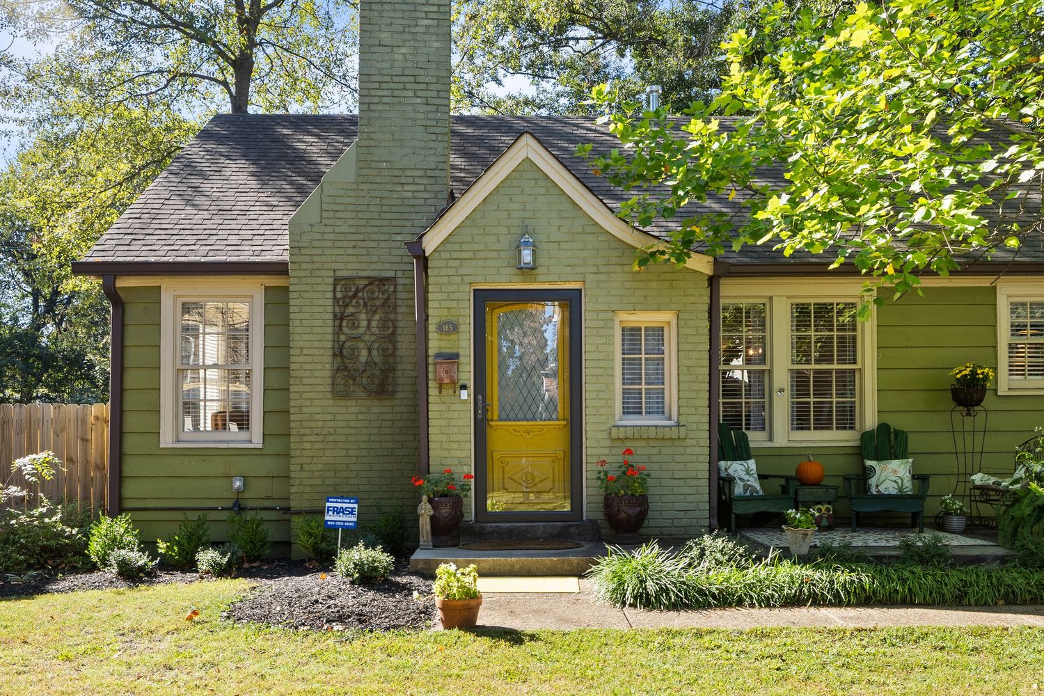 Cozy cottage with olive green exterior, yellow door, and well-maintained garden beds.