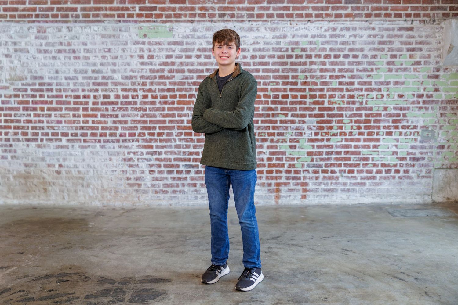 A casual pose against a rustic brick wall backdrop wearing blue jeans and sneakers.